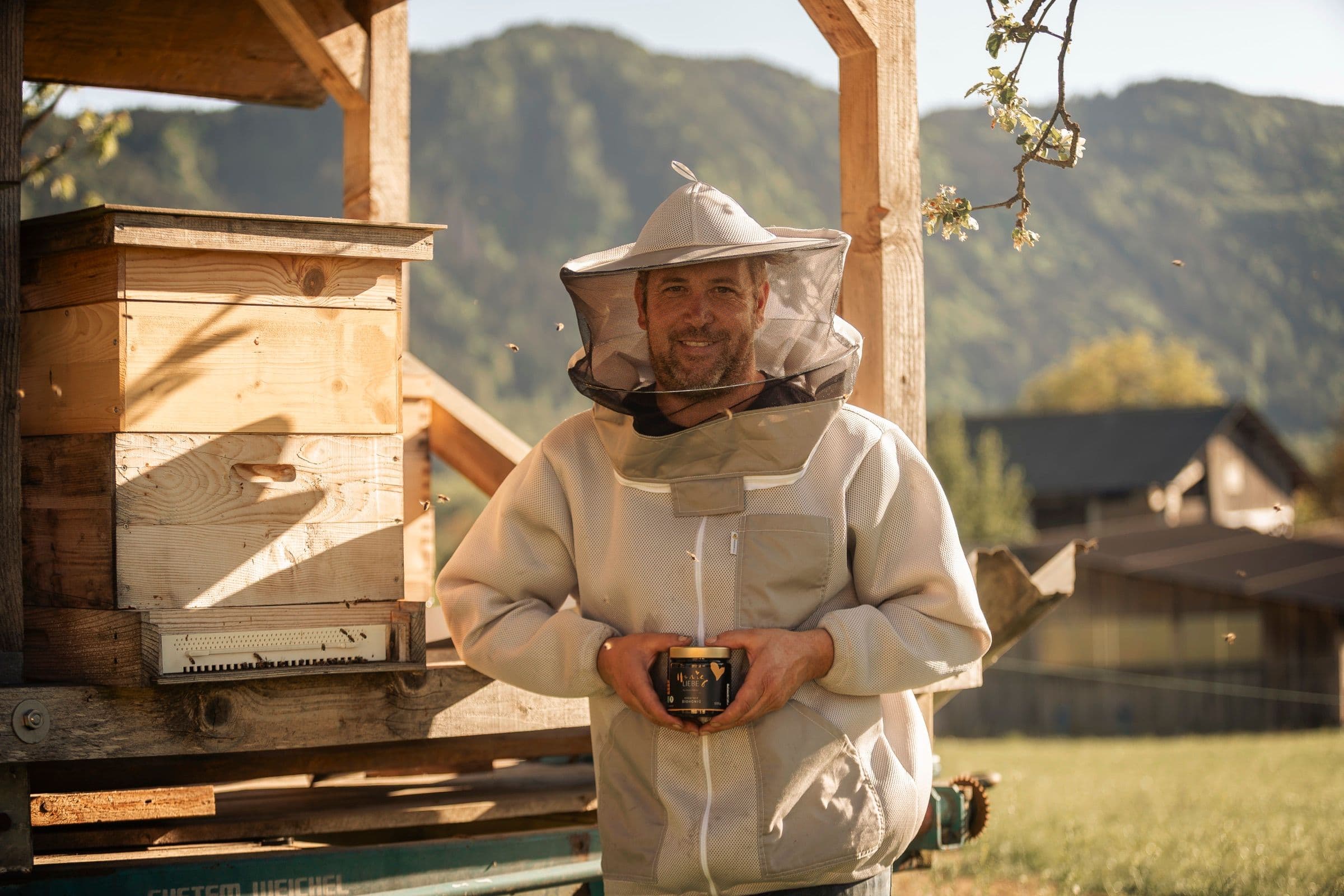 Imker Hannes Puschitz mit HonigLiebe-Glas vor den Bienenstöcken in Kärnten